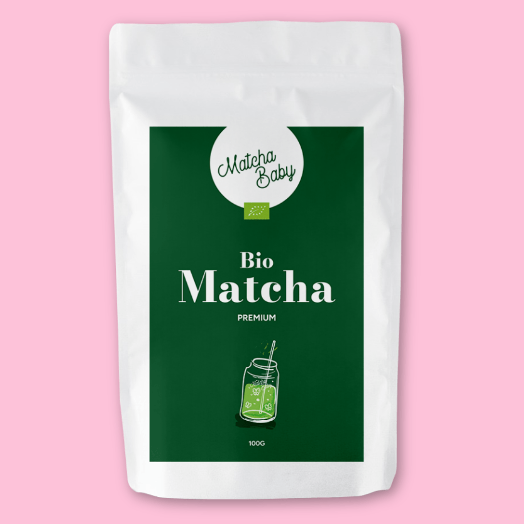 Bio Matcha Tee von Matcha Baby, 100g Packung mit grünem Etikett und stilisiertem Bild eines Matcha-Getränks im Glas mit Strohhalm, vor rosa Hintergrund.