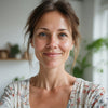 Lächelnde Frau in heller, gemütlicher Wohnung mit Pflanzen im Hintergrund; sie trägt ein helles Oberteil. Idealbild für eine Wohlfühl-Website.