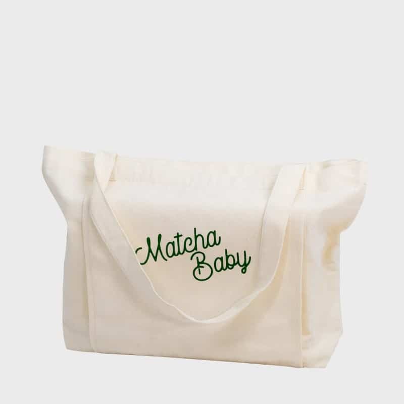 Abbildung des Jutebeutels von Matcha Baby von vorne mit Inhalt. In Grün die Aufschrift „Matcha Baby“